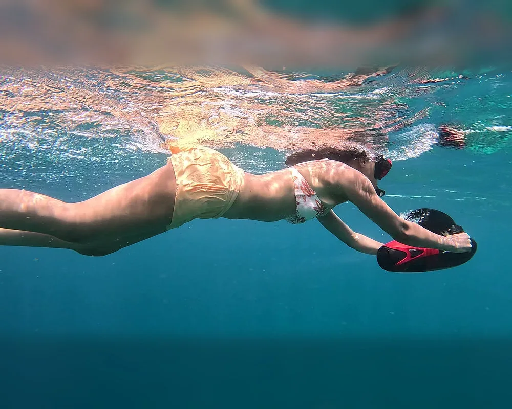 Nadador sujetando un scooter submarino rojo cerca de la superficie