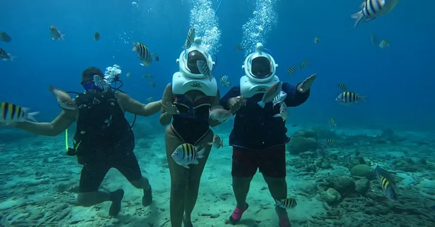 A diver beside two helmet-walking participants above the seabed
